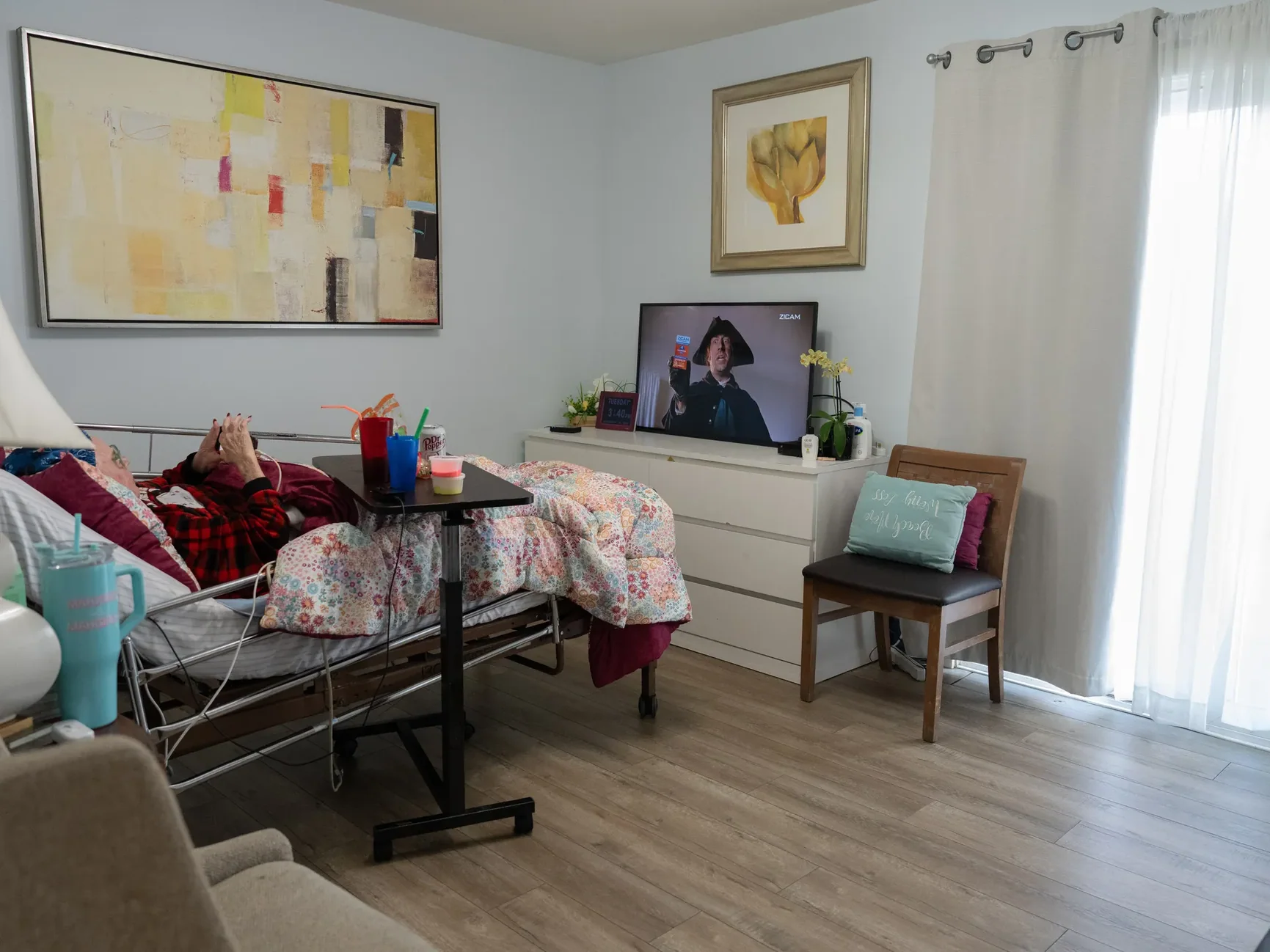 Resident enjoying television time in a comfortably furnished bedroom with hospital bed and home-like decor